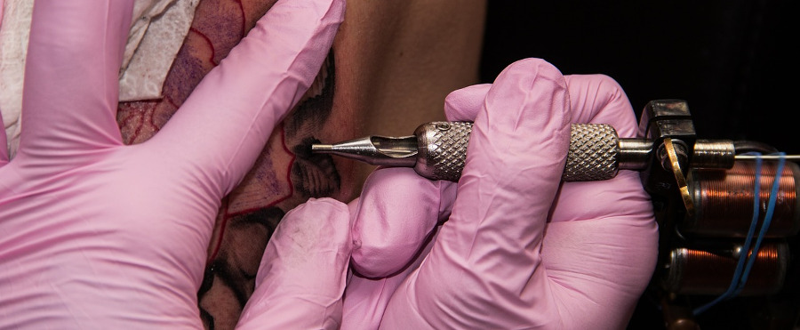 
руки мастера в розовых перчатках набивают тату клиенту